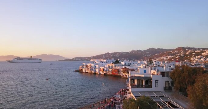 Amazing cinematic aerial shot of Little Venice, Mykonos island sunset with a lot of tourists walking and taking photos.