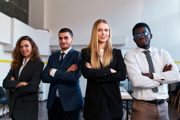 Multiracial business team stands confidently in office. Caucasian female CEO with arms crossed flanked by diverse colleagues. Professionals in suits portray unity, leadership in corporate setting.