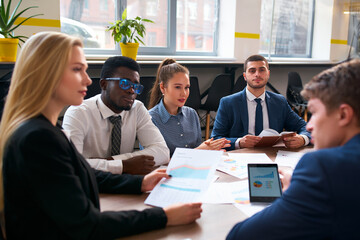 Multiracial business team with asian businesswoman and african businessman in discussion at office meeting. Group analyzes charts, diagrams on papers for project planning and strategy.