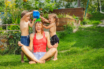 Two small siblings playfully pour water over their seated mother - 784030489