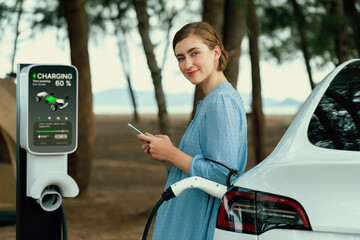 Holiday road trip vacation traveling to the beach camp with electric car, young woman checking...