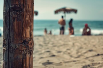 A wooden pole standing on a sandy beach with people in the background. Suitable for travel and vacation concepts