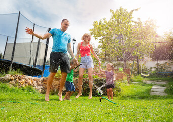 Joyful parents and kids engaged in water play outside house - 784036058