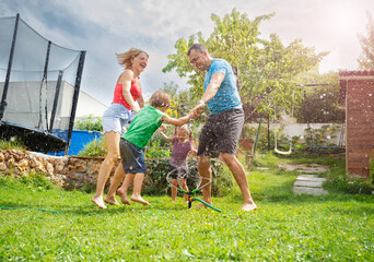 Family bonds through a spirited soaking in their green garden - 784036601