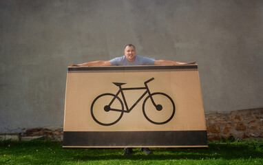 Man standing with an enormous packing box showing a bike icon - 784038035