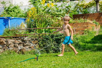 Happy boy frolics through spray of water from outdoor sprinkler - 784039649