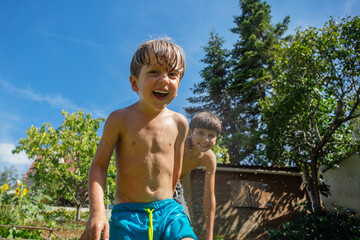 Two young boys laugh have fun, splash water in a sunny backyard - 784040220