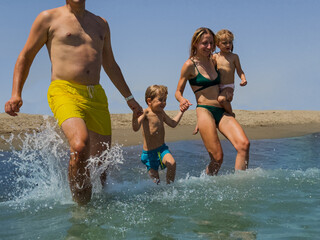 A family of four enjoys lively splash in shallow ocean waters - 784041014