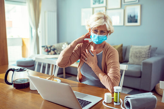 Senior woman with face mask using laptop and feeling unwell at home