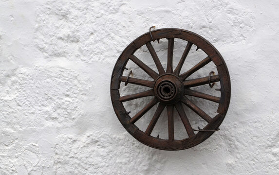 Old wooden wheel on a white stone wall background.Retro style concept for interior design with copy space.