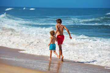 Joyful siblings race by the waterfront on a bright sandy beach - 784048201