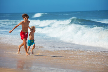 Laughing boys in a chase on sandy beach near the foamy sea waves - 784049059