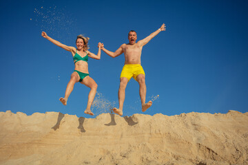 Man and woman jumping above sand dune against clear blue sky - 784055267