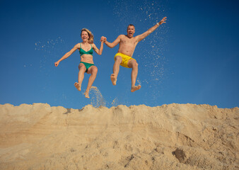 Man and woman energetically spring up from beige sand embankment - 784055658