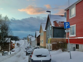 A row of parked cars covered with snow lines this residential street in Norway on a Sunday morning.