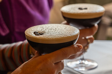 A close up of hands holding espresso martini cocktails, with a shallow depth of field