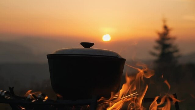 Beautiful sunset in the mountains. Against the background of the sunset, a hearth is burning, on which a cauldron of food is being cooked.