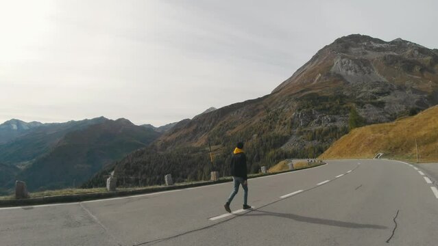 Tourist man walking on center of mountain road on sunset. Joyful guy having adventure in mountains.