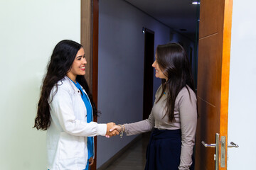 female doctor or dentist shaking hands with latin hispanic woman patient at medical or dentistry clinic. Thank you concept.