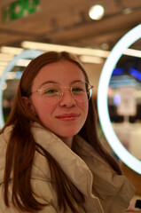 A woman wearing glasses and a white jacket is smiling at the camera