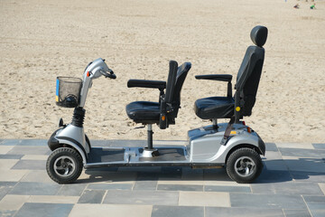 Mobility scooter parked on pavement road near sandy beach on sunny day - obrazy, fototapety, plakaty