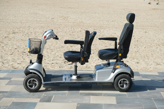 Fototapeta Mobility scooter parked on pavement road near sandy beach on sunny day