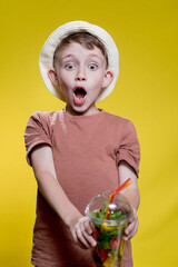 Cute boy with Mojito cocktail from plastic cup over yellow background