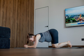 Happy pregnant woman stretching on mat at home.