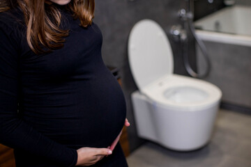 Incontinence and frequent urination during pregnancy. Pregnant woman need to pee standing by toilet in bathroom. Pregnancy concept image. Health and wellbeing of expectant mother