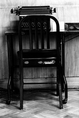 Cadeira de ferro em mesa de madeira e máquina de escrever.  - obrazy, fototapety, plakaty