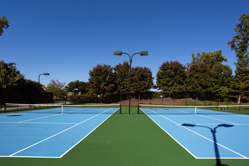 Outdoor Tennis Court with A Vibrant Blue Playing Surface and Surrounding Greenery Under a Clear Blue Sky