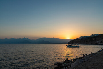 Fototapeta premium ANTALYA, TURKYE - SEPTEMBER 17, 2022: Old harbour in Antalya at sunset with tourists boat at front