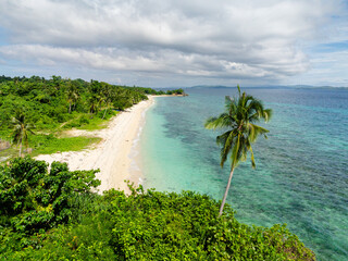 Tropical beach with clear water waves. Coconut trees in coastline. Carabao Island. San Jose,...