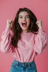 Joyful woman in pink sweater cheering with clenched fists on a vibrant pink backdrop - obrazy, fototapety, plakaty