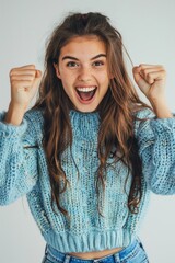 Joyful female with a bright smile, fists pumped in victory on a light background - obrazy, fototapety, plakaty
