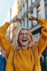 Vibrant young woman in yellow sweater triumphantly raises arms in city setting