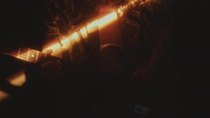 Man in open shirt playing electric guitar while performing rock music concert in dark room with shining light beam. Shaky cam, midsection shot