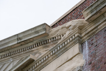Obraz premium Example of crumbling, deteriorating ornamental precast concrete elements, features, on an old brick school building.