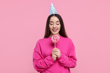 Woman in party hat holding lollipop on pink background