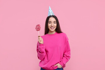 Woman in party hat holding lollipop on pink background