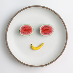 Fruit face. Fruit emotions. Mini watermelons and banana on a plate. Miniature fruit figures made of polymer clay. Summer.