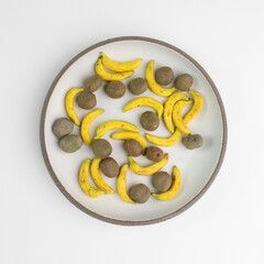 Miniature bananas and kiwi in a round plate on a white background. Figures made of polymer clay....