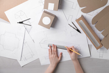 Woman creating packaging design at light wooden table, top view