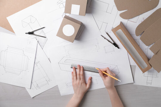 Woman creating packaging design at light wooden table, top view