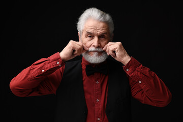 Senior man touching mustache on black background