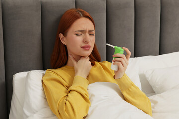 Young woman holding throat spray in bed