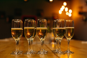Champagne Glasses on Bar Counter with Warm Ambient Light. Row of champagne glasses filled with sparkling wine, garnished with lime, set on a wooden bar counter against a backdrop of soft glowing light