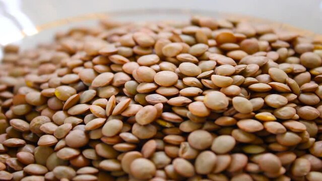 Pouring raw lintel seeds in white plate close up 1