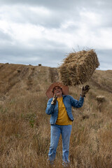 A Latina woman working in the field, lifting a hay bale in the middle of a cut grass field
