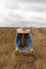 Unrecognizable woman, covered by her sun hat, ready to lift a hay bale in the meadow of the Andes mountains